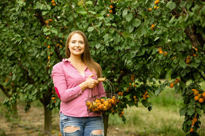 Smiling woman holding fruit against plants