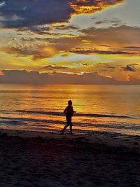 Silhouette woman on beach against sky during sunset