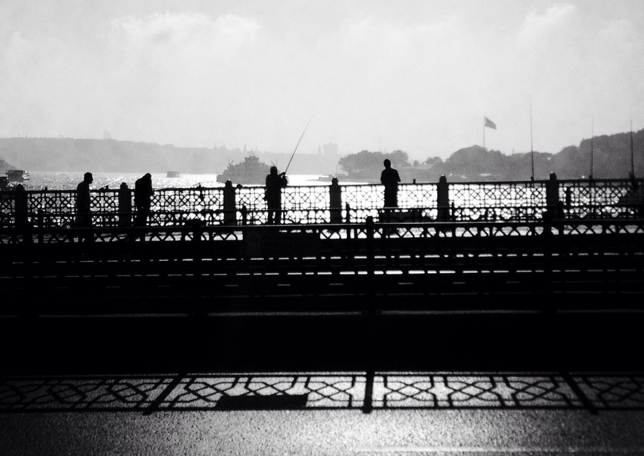 railing, lifestyles, men, leisure activity, silhouette, person, walking, sky, bridge - man made structure, full length, connection, medium group of people, standing, togetherness, water, rear view