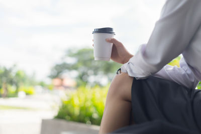 Midsection of woman holding coffee cup against sky