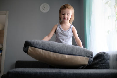 Kid toddler builds house from pillows on sofa in living room, lifestyle and games in real interior