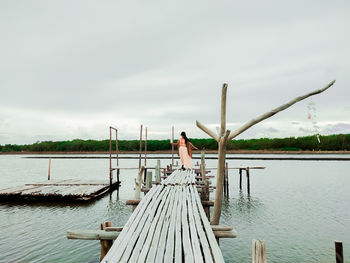 Woman standing on pier by lake against sky