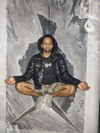 Portrait of young man sitting against wall