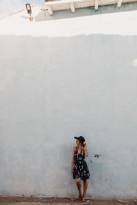 Woman in hat standing against house