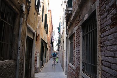 Rear view of woman walking on narrow alley amidst buildings