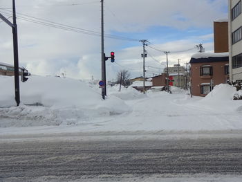 Snow covered road by buildings against sky