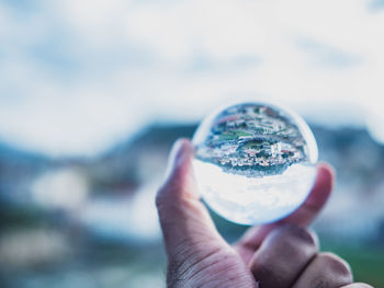 Close-up of hand holding crystal ball against sky