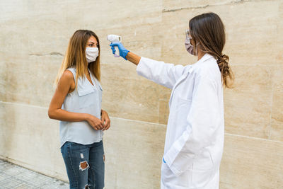 Young woman holding hands standing against wall