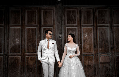 Newlywed couple holding hands while standing against wall