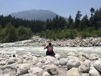 Man sitting on rock against waterfall