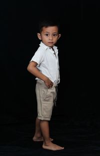 Portrait of boy standing against black background