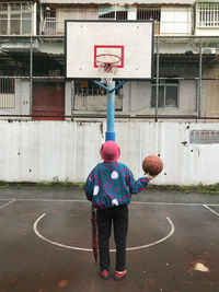 Full length rear view of woman playing basketball at court