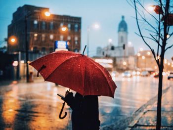 Person carrying umbrella standing on city street during rainy season