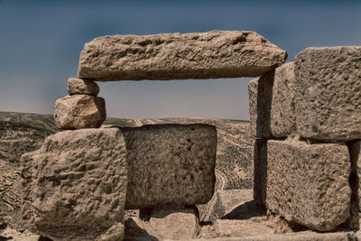 Stone wall by rocks against sky