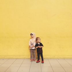 Full length of cute girl standing against yellow wall