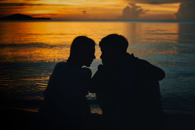 Silhouette couple standing by sea against sky during sunset