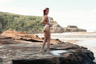 Woman standing on rock by sea against sky