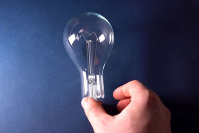 Cropped hand by light bulb against blue background