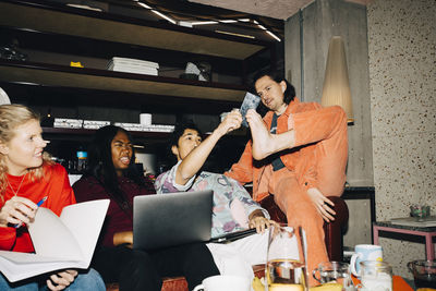 Male entrepreneur holding smart phone with leg while coworkers sitting in creative office