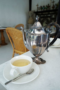 Stainless steel teapot with a ceramic porcelain cup of hot tea