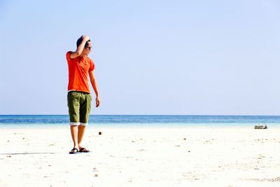 Full length of young man walking at beach against clear sky during sunny day