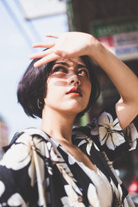 Woman looking away while shielding eyes in city