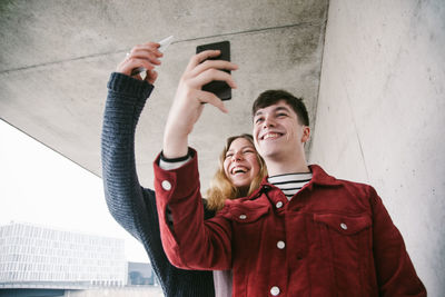 Young man using mobile phone while standing against wall