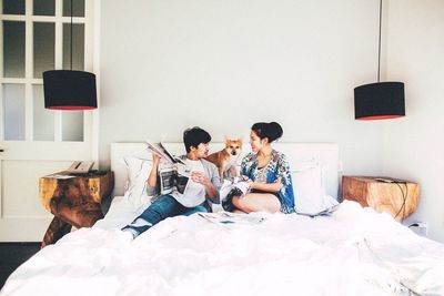 Man and woman with newspaper sitting by dog on bed at home