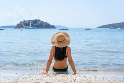 Young girl from the back in a straw hat on the background of the sea bay