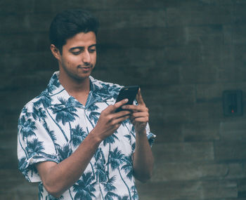 Smiling young man using mobile phone while standing outdoors