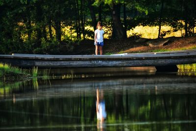 Child standing on bridge looking into pond 