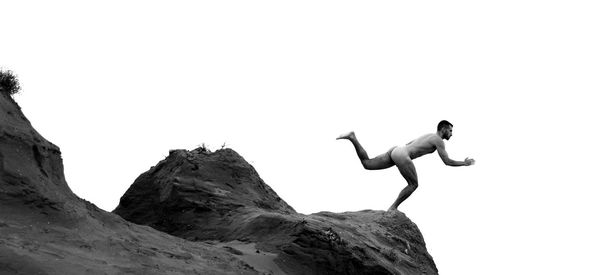 Full length of shirtless man jumping on rock against clear sky