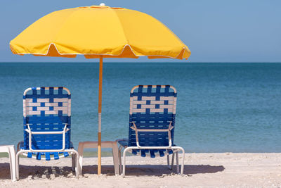 Deck chairs on beach against sky