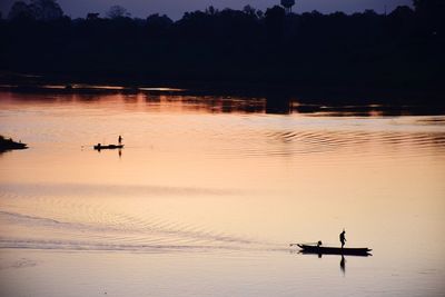 Silhouette people on lake against sky during sunset