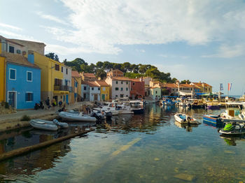 Boats moored in canal by buildings in city against sky