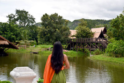 Rear view of women on lake by trees against sky