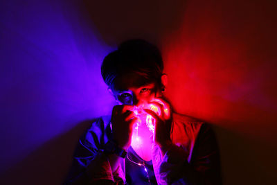 Portrait of man holding illuminated lighting equipment in darkroom