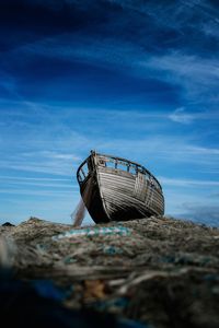 Low angle view of abandoned boat on beach against blue sky