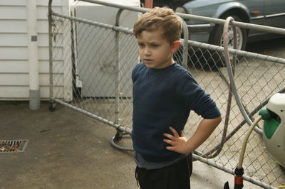 Boy with hand on hip looking away while standing by railing