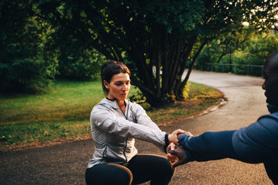 Male and female athletes holding hands while practicing chair position on road