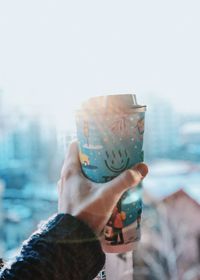 Close-up of hand holding drink against sky