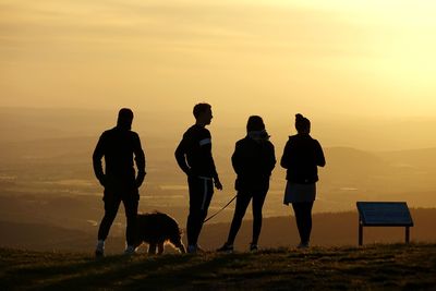 Silhouette people walking on land against sky during sunset