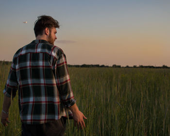 Young man standing on field against sky during sunset