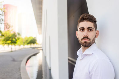 Portrait of a bearded man leaning on white wall looking aside