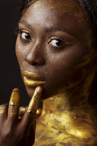 Close-up portrait of young woman with golden glitter against black background