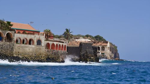 Buildings by sea against clear blue sky