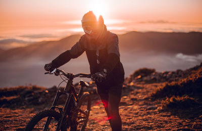 Side view of guy in helmet riding on bicycle on top of mountain with beautiful sunset