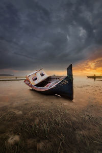 Abandoned ship on beach against sky during sunset