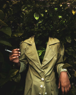 Midsection of man holding mobile phone while standing against plants