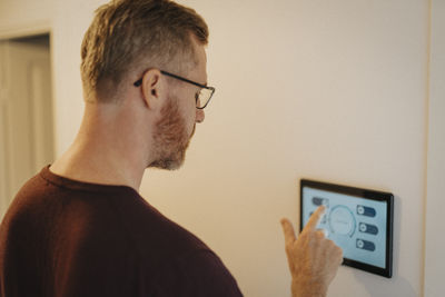 Mature man using digital tablet mounted on wall at smart home